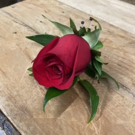 Single red rose boutonniere with green leaves on a wooden surface