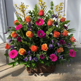 Basket arrangement of orange roses, pink gerberas, and purple flowers