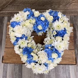 Heart-shaped floral wreath with white and blue flowers on a wooden surface