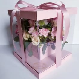 Pink roses and carnations in a clear gift box with a ribbon bow