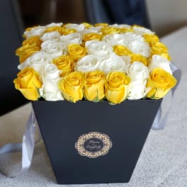 Yellow and white roses arranged in a black box with a ribbon
