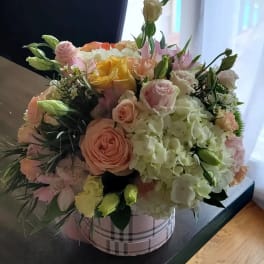 Mixed bouquet of pastel roses and hydrangeas in a plaid round box