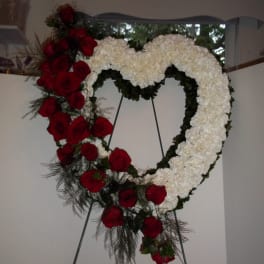 Heart-shaped floral wreath with red roses and white flowers on an easel