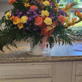 Colorful mixed flower arrangement in a white bucket with a ribbon