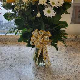 Yellow roses and white daisies in a clear glass vase with a yellow ribbon