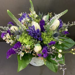 Compact arrangement of purple, white, and green flowers in a small marble-pattern ceramic vase
