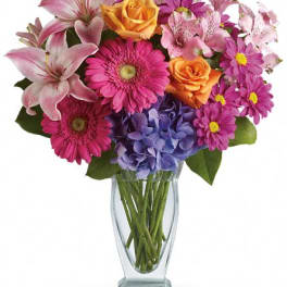Mixed bouquet of pink lilies, roses, gerbera daisies, and hydrangea in a glass vase