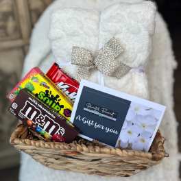 Gift basket with a white plush blanket, candy boxes, and a florist card