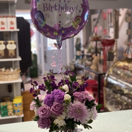 Purple flower arrangement with a Happy Birthday balloon in a glass vase