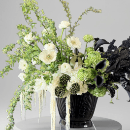 Black vase with white and green floral arrangement and black calla lilies