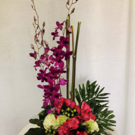 Tall floral arrangement with purple orchids and pink blooms in a low container