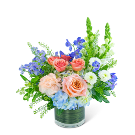 Mixed bouquet of peach roses, blue flowers, and white blooms in a glass vase