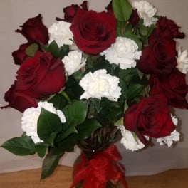Bouquet of red roses and white carnations in a glass vase with a red ribbon