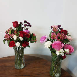 Two mixed flower bouquets in clear glass vases on a wooden table