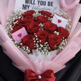 Bouquet of red roses with baby’s breath, pink wrap, and Valentine card