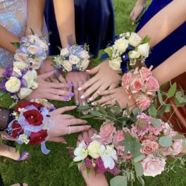 Hands holding small floral wrist corsages in assorted colors on grass