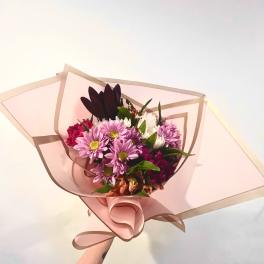 Handheld bouquet of pink and purple daisies wrapped in blush paper