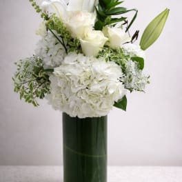 White roses and hydrangeas arranged in a tall glass vase
