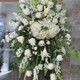 Large white funeral spray with roses, lilies, and hanging blooms on an easel
