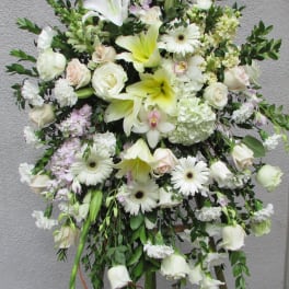 Large white funeral spray with roses, lilies, and gerbera daisies on a stand