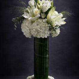White lilies and hydrangeas arranged in a tall green vase