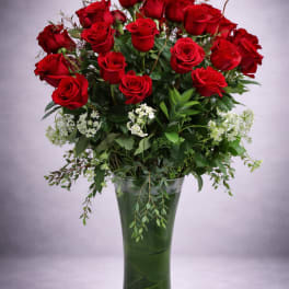 Red roses arranged in a tall glass vase with white filler flowers