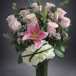 Pink lilies and roses arranged with white hydrangea in a glass vase