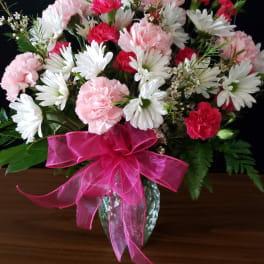 Pink and red carnations with white daisies in a clear vase with a bright pink bow