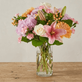 Mixed bouquet of pink lilies, lavender mums, white roses and peach blooms in a clear glass vase