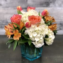 Bouquet of orange and pink roses with white hydrangeas in a blue vase