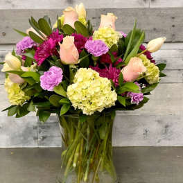 Mixed bouquet of roses, hydrangeas, and tulips in a clear glass vase