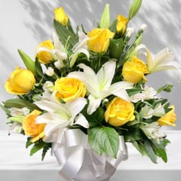 Yellow roses and white lilies in a white vase with a ribbon