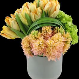 Yellow tulips and peach flowers arranged in a white vase