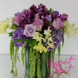Lavender roses and purple flowers in a glass vase with trailing green accents
