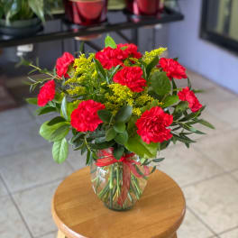 Red carnations in a glass vase with yellow filler flowers