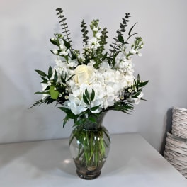 White floral arrangement in a clear glass vase with tall greenery