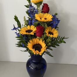 Sunflowers, red roses, and blue flowers arranged in a dark blue vase