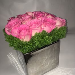 Pink roses arranged in a square silver vase with green moss