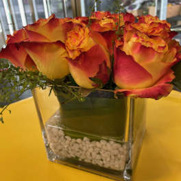 Orange and red roses arranged in a square glass vase