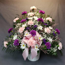 Pink and purple floral arrangement in a white basket with a pink ribbon