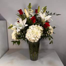 Red roses and white lilies in a tall glass vase with white hydrangeas