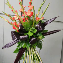 Tall bouquet of coral gladiolus with dark ribbon accents