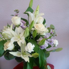White lilies and roses arranged in a glass vase with lavender accents.