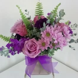 Pink and purple bouquet in a clear vase with a purple ribbon