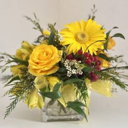 Yellow roses and a gerbera daisy in a glass vase with red berries