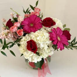 Bouquet of red roses, pink gerberas, and white hydrangeas in a glass vase