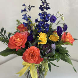 Colorful bouquet of roses and blue delphinium in a glass vase