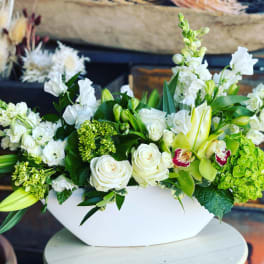 White and green floral arrangement in a white bowl vase