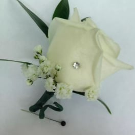 White rose boutonniere with small white blossoms and green leaves