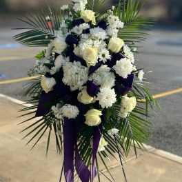 White floral standing spray with purple ribbon accents and palm fronds